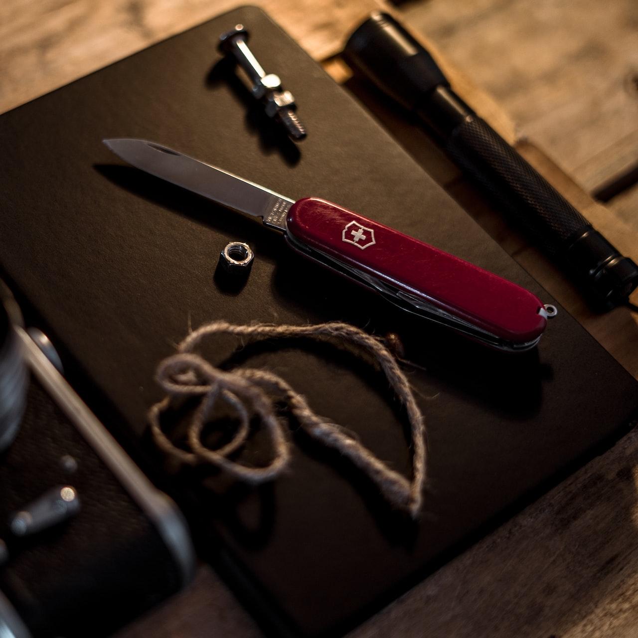 red and silver pocket knife beside black and silver camera lens